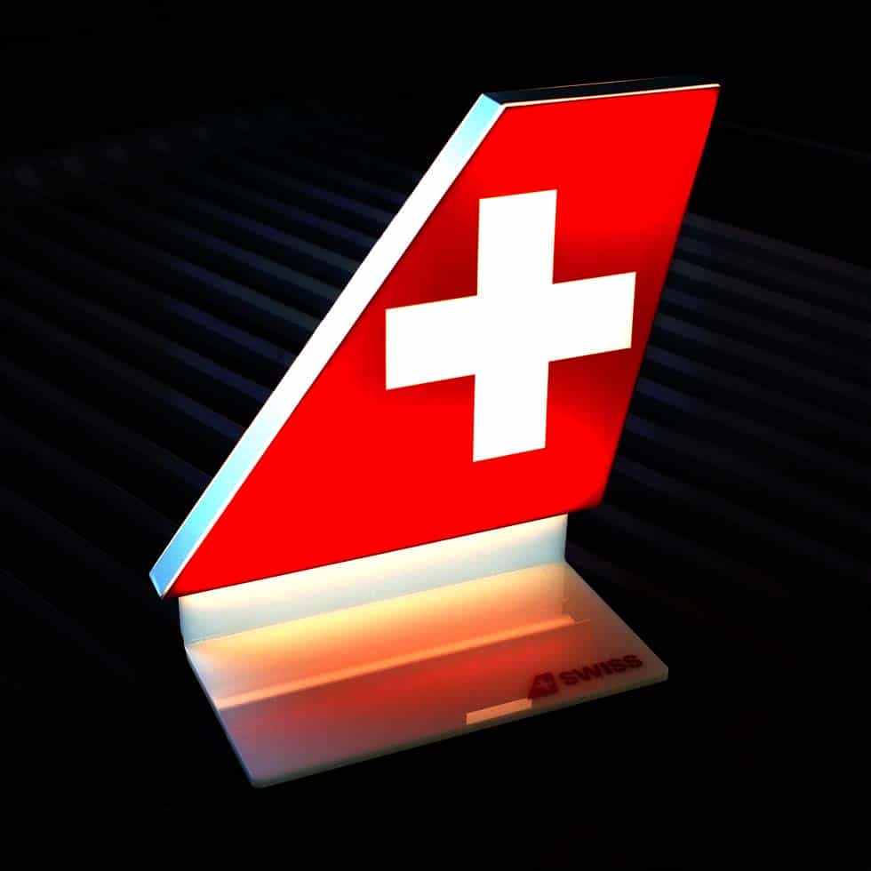 Prémium minőségű, világító asztali display a légitársaság vörös alapon fehér keresztet formázó logójával sötét háttér előtt.