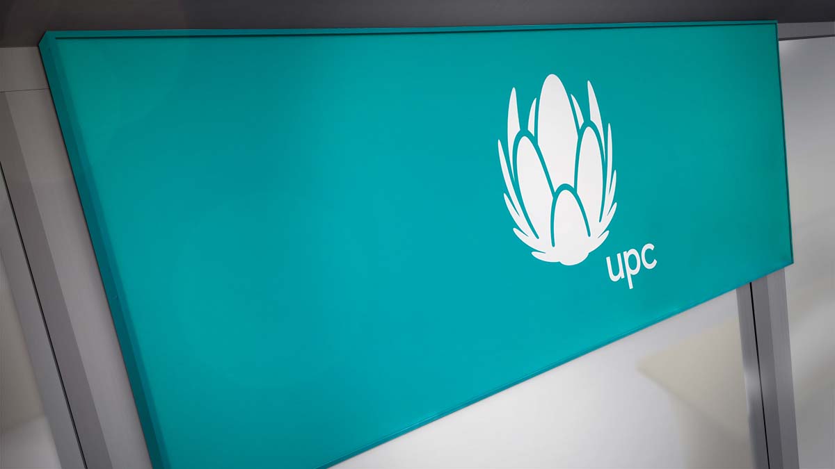 Akvamarín színű letisztult fém és plexi világítótábla az UPC nagyméretű fehér logójával a közepén.