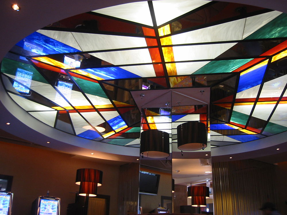 Színes, centrálisan geometrizáló, kör alakú üvegmennyezet egy kaszinó belső terében.